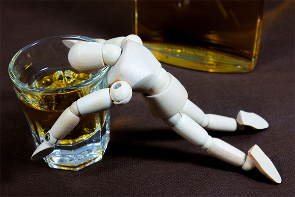 Our motor skills are impaired by the effect of alcohol on a structure in our brain called the cerebellum. A wooden figure of a man leaning on a glass of whisky | Shutterstock, shutter_tonko