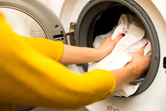 Shorter and colder cycles of washing could keep clothes in better condition. A woman inserting laundry into a washing machine | Photo: Arturs Budkevics, Shutterstock